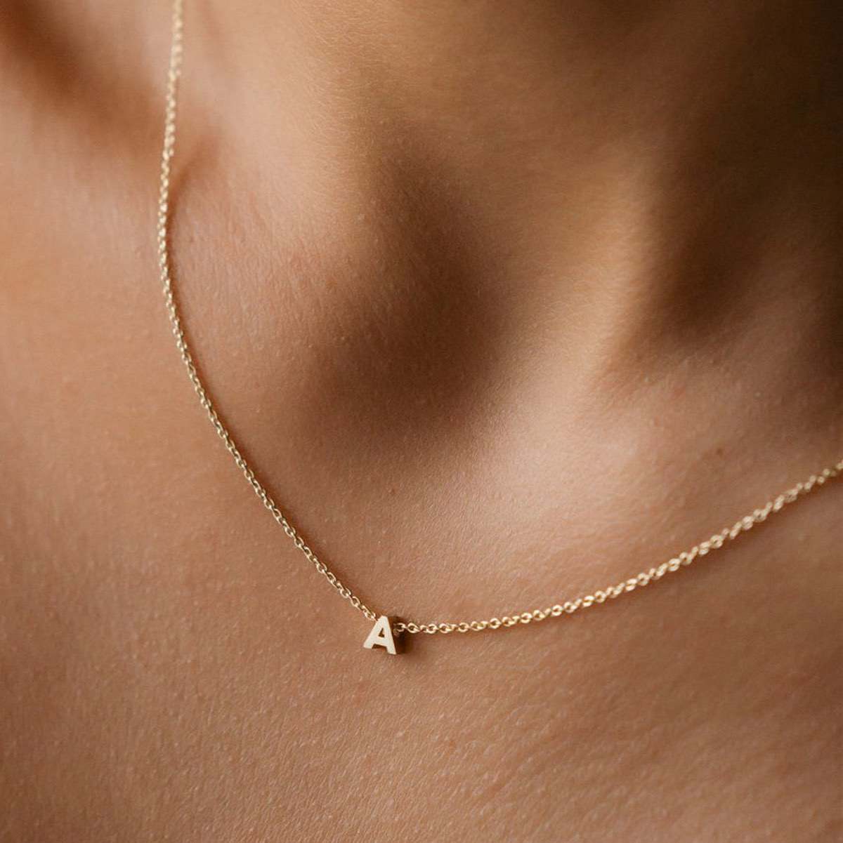 Hand finished solid gold letter necklace: Close up of a model wearing our beautiful 9ct yellow gold Tiny Letter A Charm Necklace with a 40cm cable chain