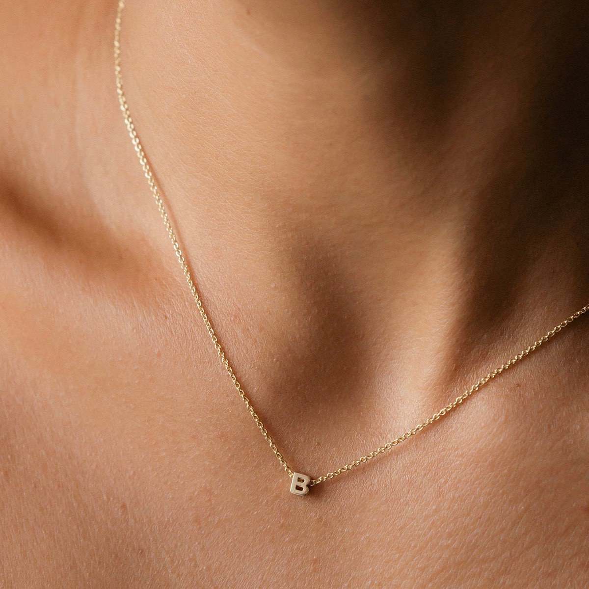Hand finished solid gold letter necklace: Close up of a model wearing our beautiful 9ct yellow gold Tiny Letter B Charm Necklace with a 40cm cable chain