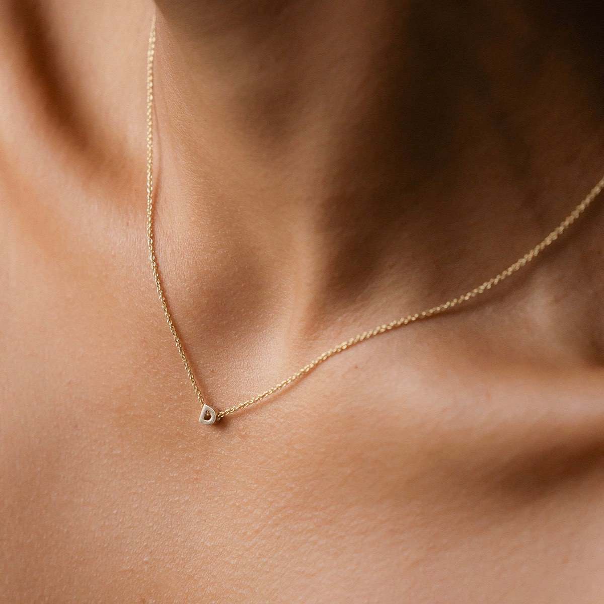 Hand finished solid gold letter necklace: Close up of a model wearing our beautiful 9ct yellow gold Tiny Letter D Charm Necklace with a 40cm cable chain