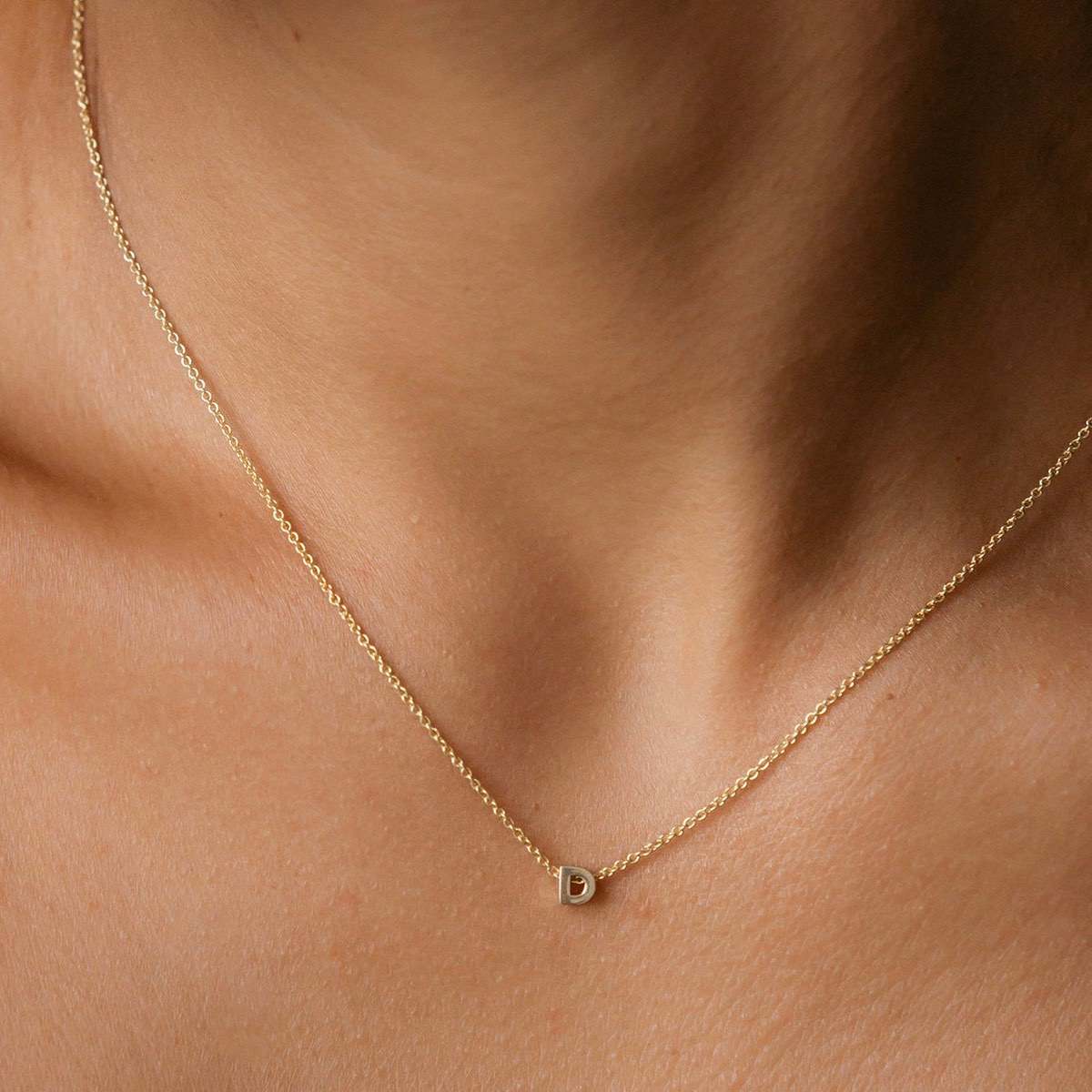 Hand finished solid gold letter necklace: Close up of a model wearing our beautiful 9ct yellow gold Tiny Letter D Charm Necklace with a 40cm cable chain
