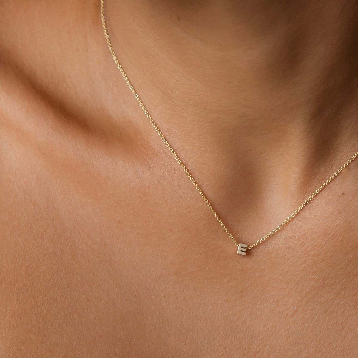 Hand finished solid gold letter necklace: Close up of a model wearing our beautiful 9ct yellow gold Tiny Letter E Charm Necklace with a 40cm cable chain