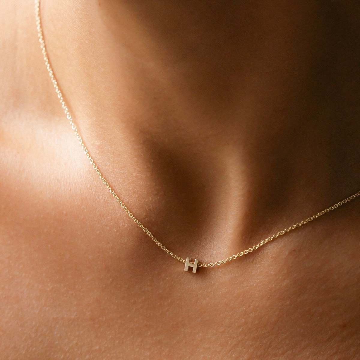Hand finished solid gold letter necklace: Close up of a model wearing our beautiful 9ct yellow gold Tiny Letter H Charm Necklace with a 40cm cable chain