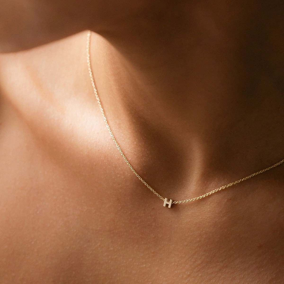 Hand finished solid gold letter necklace: Close up of a model wearing our beautiful 9ct yellow gold Tiny Letter H Charm Necklace with a 40cm cable chain