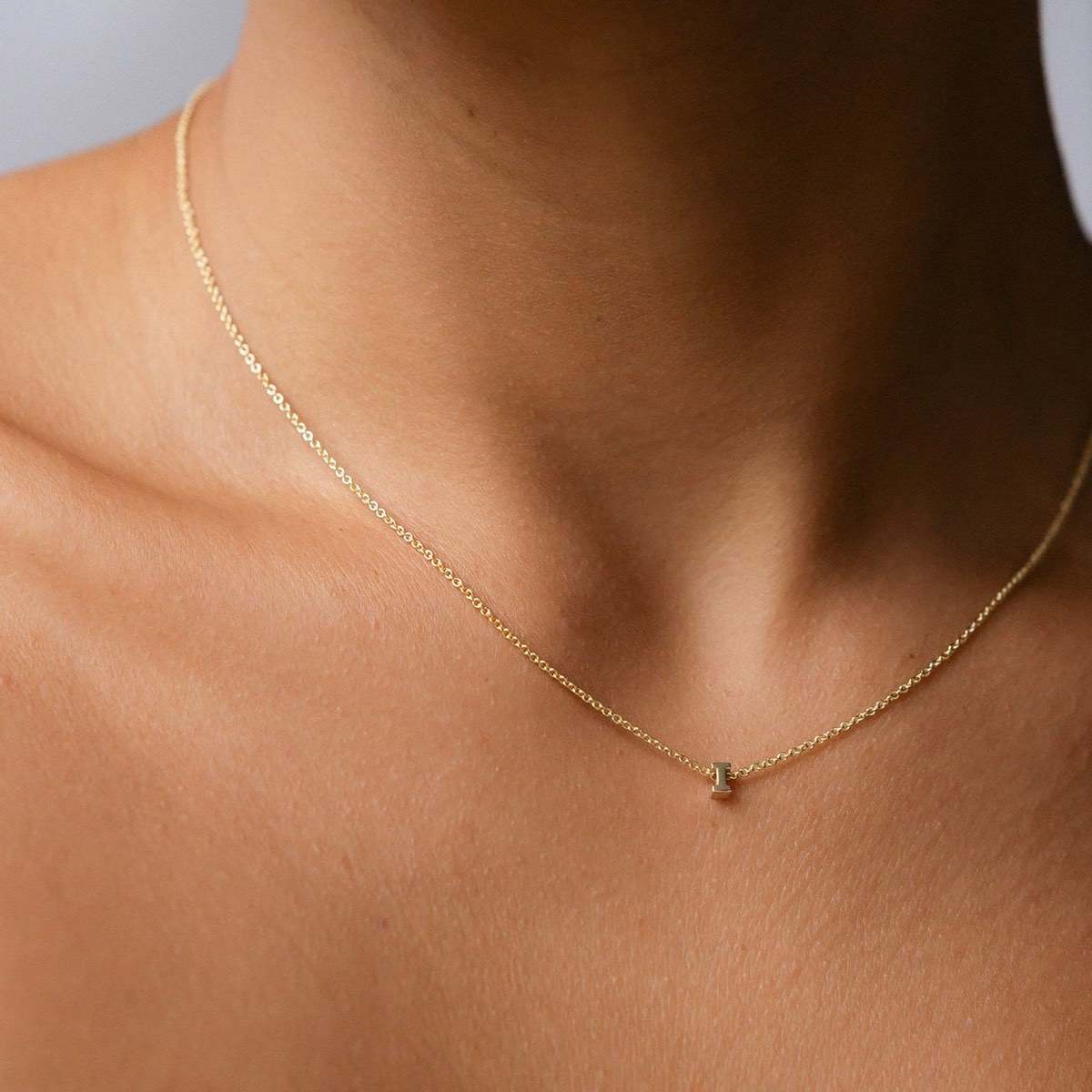 Hand finished solid gold letter necklace: Close up of a model wearing our beautiful 9ct yellow gold Tiny Letter I Charm Necklace with a 40cm cable chain