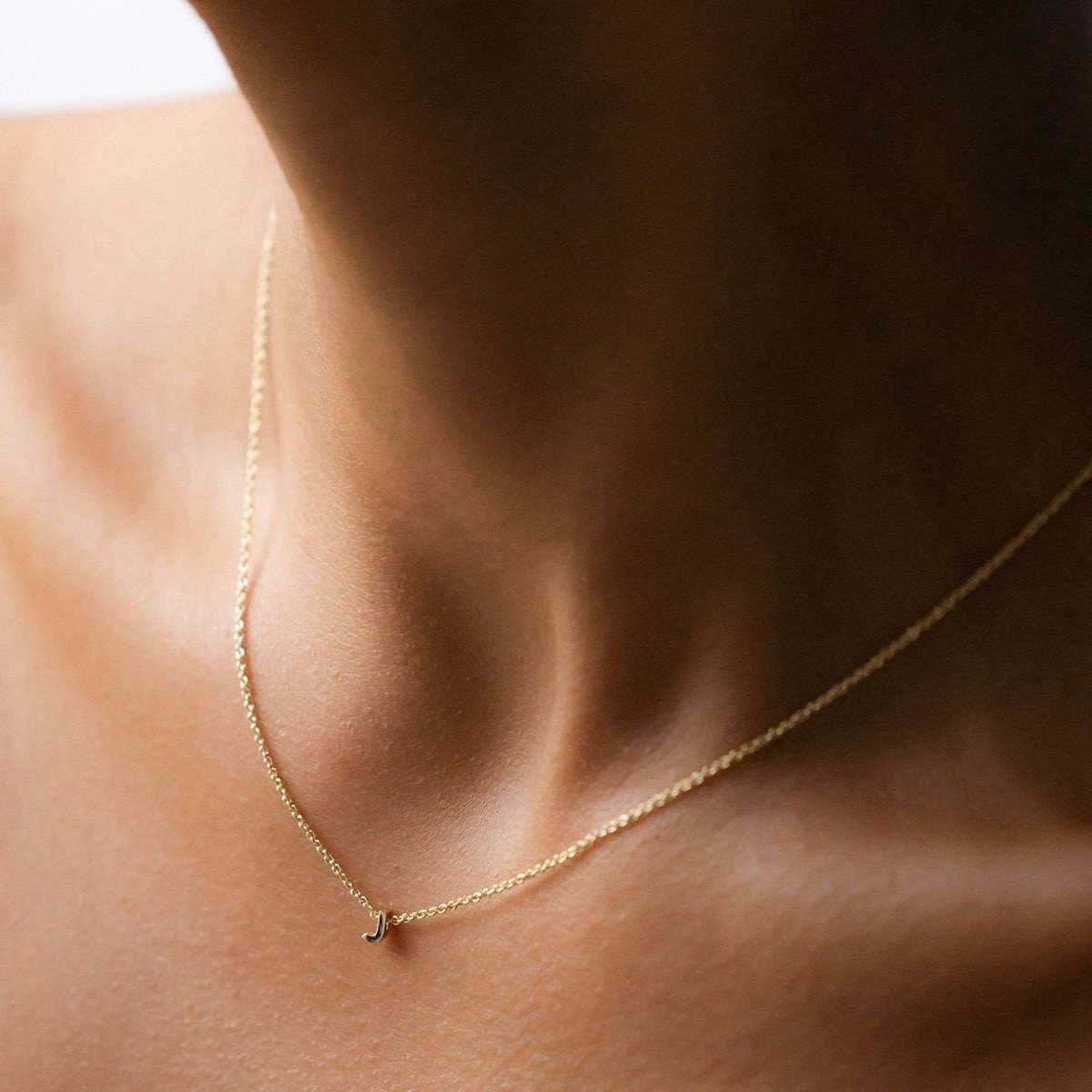 Hand finished solid gold letter necklace: Close up of a model wearing our beautiful 9ct yellow gold Tiny Letter J Charm Necklace with a 40cm cable chain