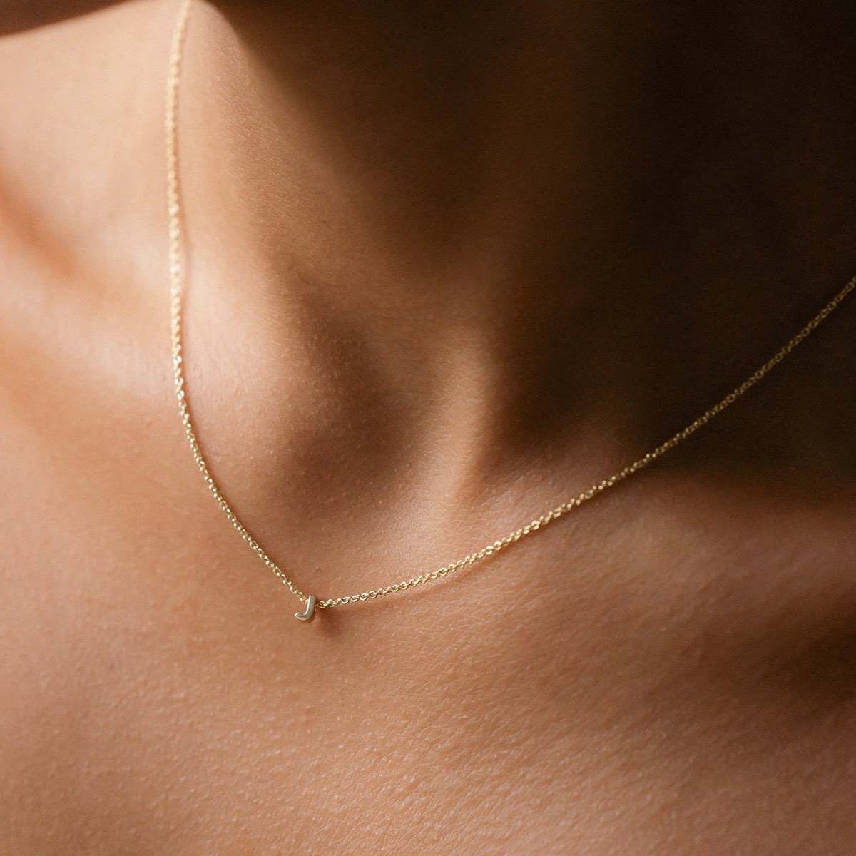 Hand finished solid gold letter necklace: Close up of a model wearing our beautiful 9ct yellow gold Tiny Letter J Charm Necklace with a 40cm cable chain