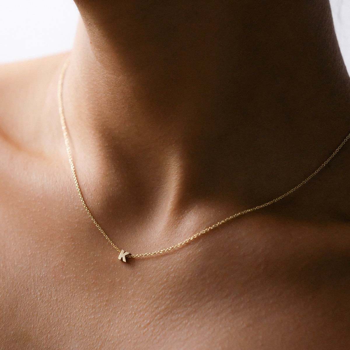Hand finished solid gold letter necklace: Close up of a model wearing our beautiful 9ct yellow gold Tiny Letter K Charm Necklace with a 40cm cable chain