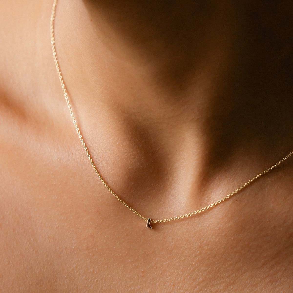 Hand finished solid gold letter necklace: Close up of a model wearing our beautiful 9ct yellow gold Tiny Letter L Charm Necklace with a 40cm cable chain