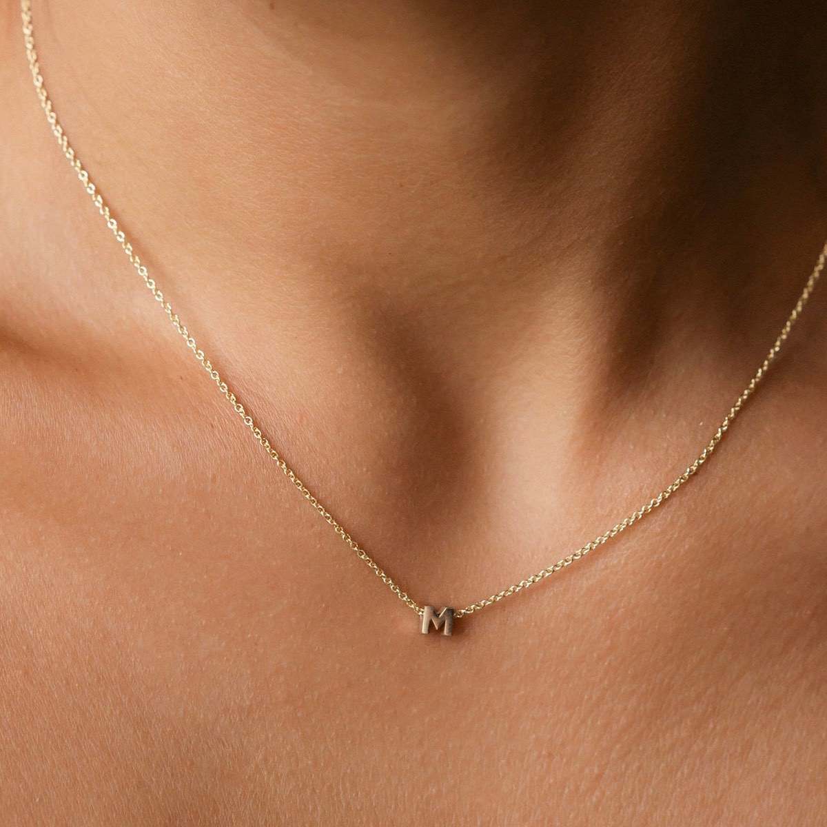 Hand finished solid gold letter necklace: Close up of a model wearing our beautiful 9ct yellow gold Tiny Letter M Charm Necklace with a 40cm cable chain