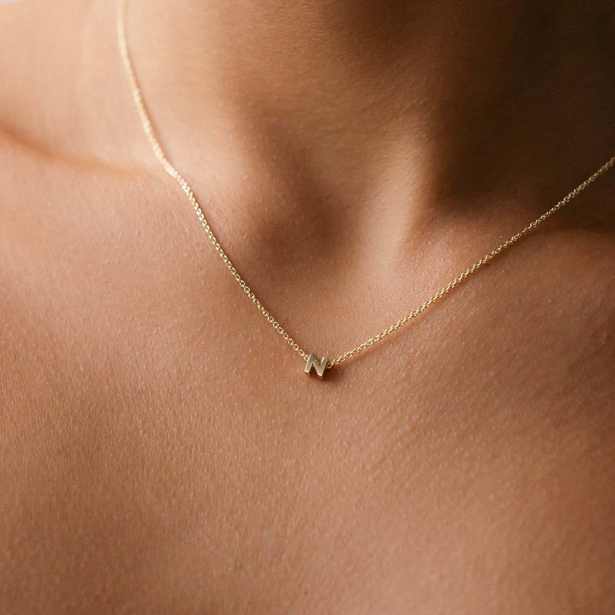 Hand finished solid gold letter necklace: Close up of a model wearing our beautiful 9ct yellow gold Tiny Letter N Charm Necklace with a 40cm cable chain