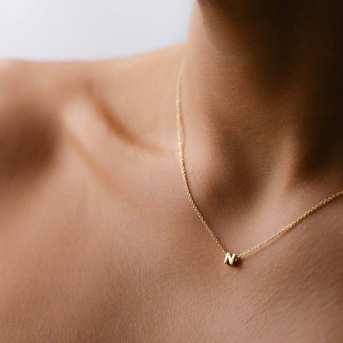 Hand finished solid gold letter necklace: Close up of a model wearing our beautiful 9ct yellow gold Tiny Letter N Charm Necklace with a 40cm cable chain