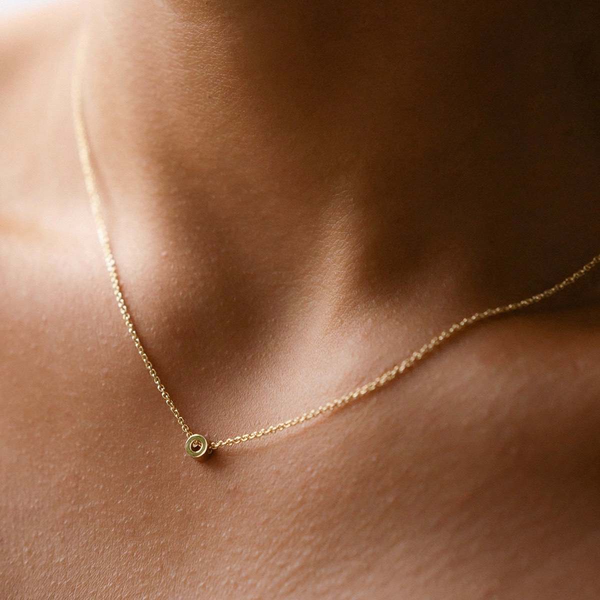Hand finished solid gold letter necklace: Close up of a model wearing our beautiful 9ct yellow gold Tiny Letter O Charm Necklace with a 40cm cable chain