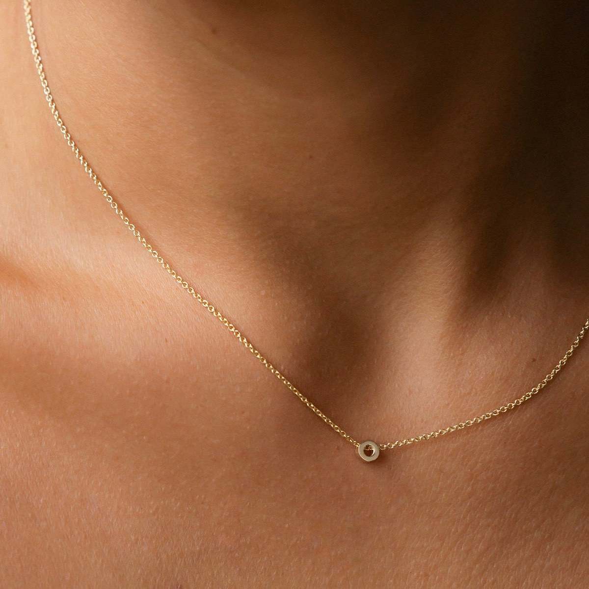 Hand finished solid gold letter necklace: Close up of a model wearing our beautiful 9ct yellow gold Tiny Letter O Charm Necklace with a 40cm cable chain