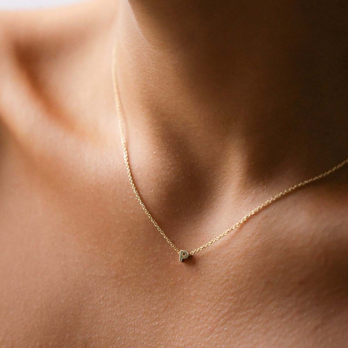 Hand finished solid gold letter necklace: Close up of a model wearing our beautiful 9ct yellow gold Tiny Letter P Charm Necklace with a 40cm cable chain