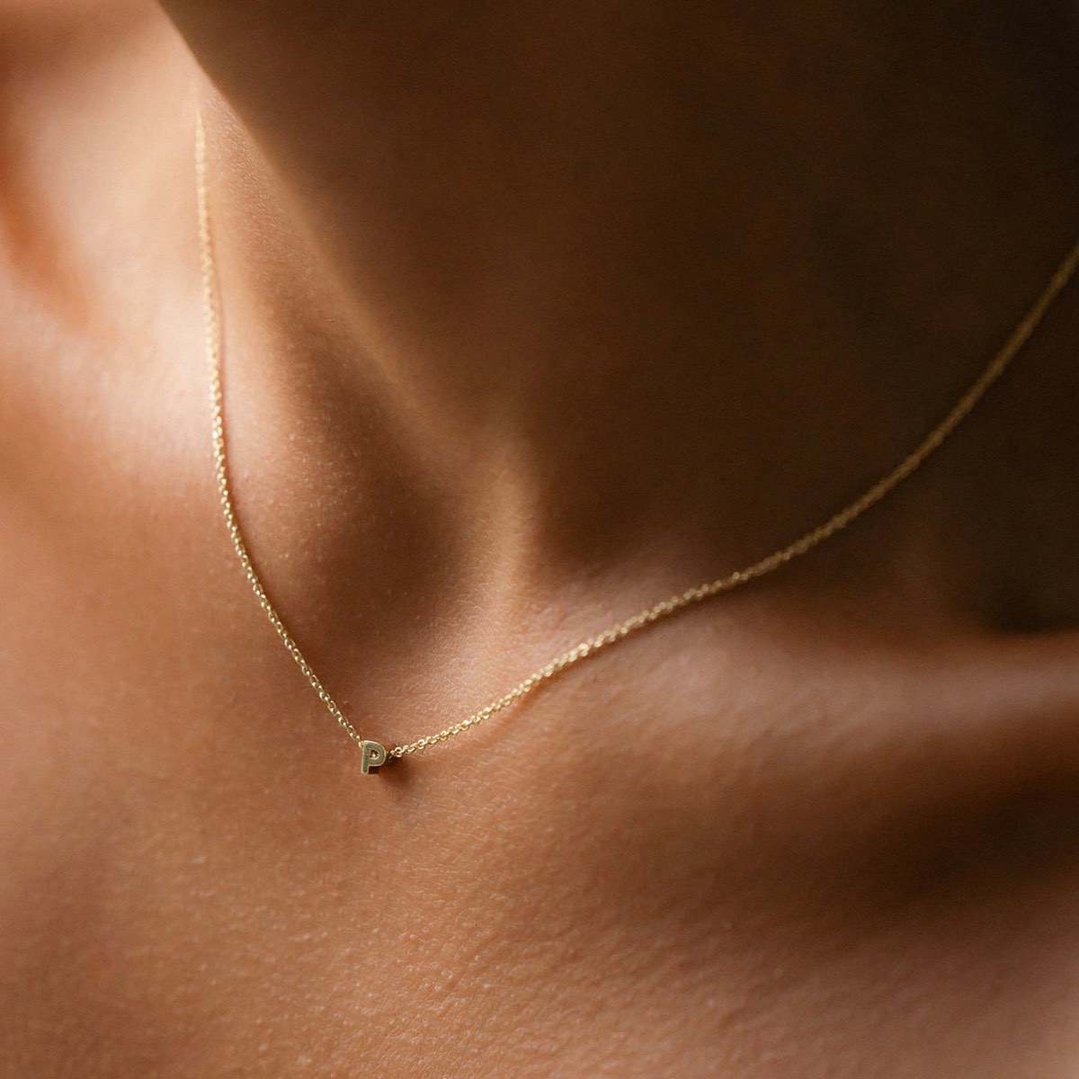 Hand finished solid gold letter necklace: Close up of a model wearing our beautiful 9ct yellow gold Tiny Letter P Charm Necklace with a 40cm cable chain