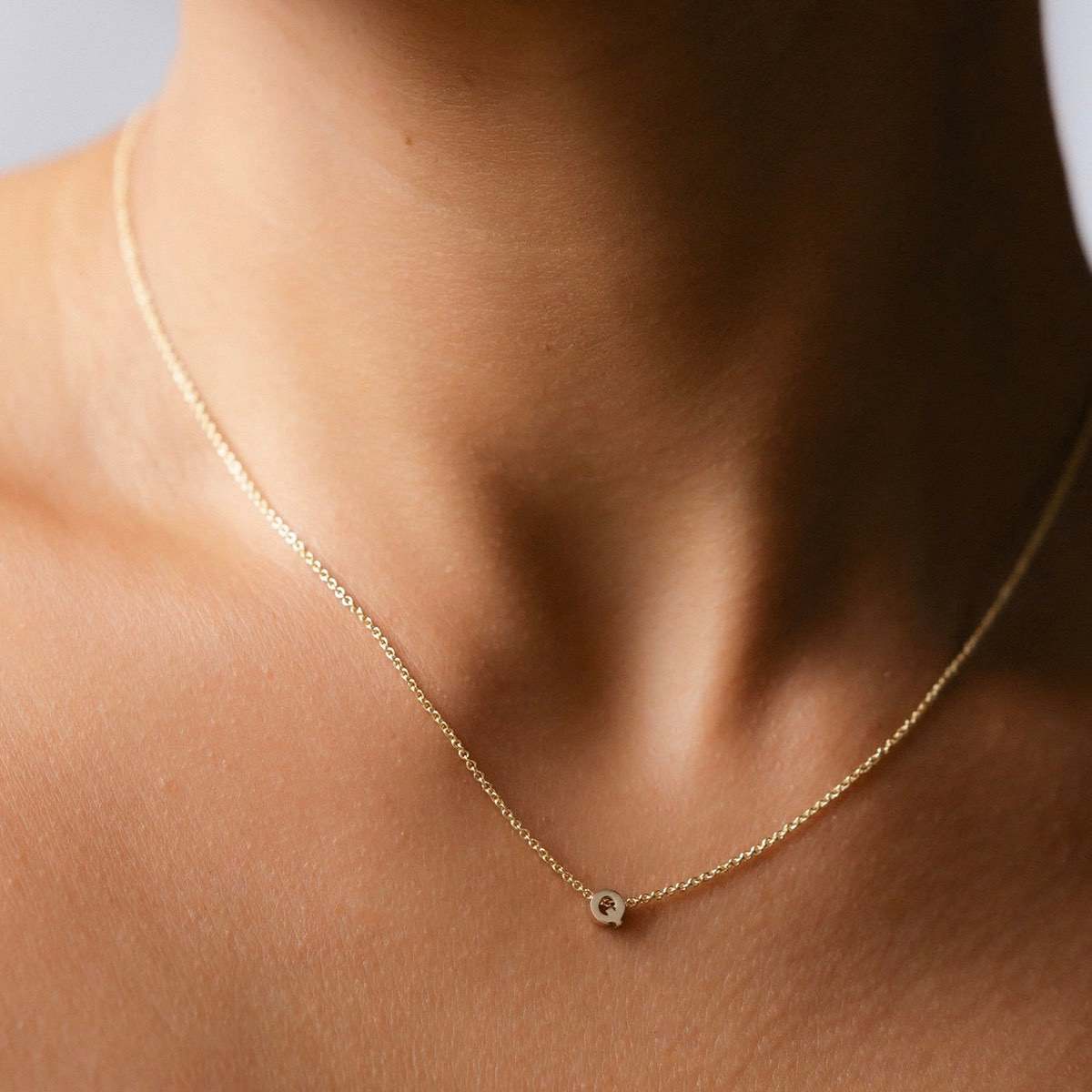 Hand finished solid gold letter necklace: Close up of a model wearing our beautiful 9ct yellow gold Tiny Letter Q Charm Necklace with a 40cm cable chain