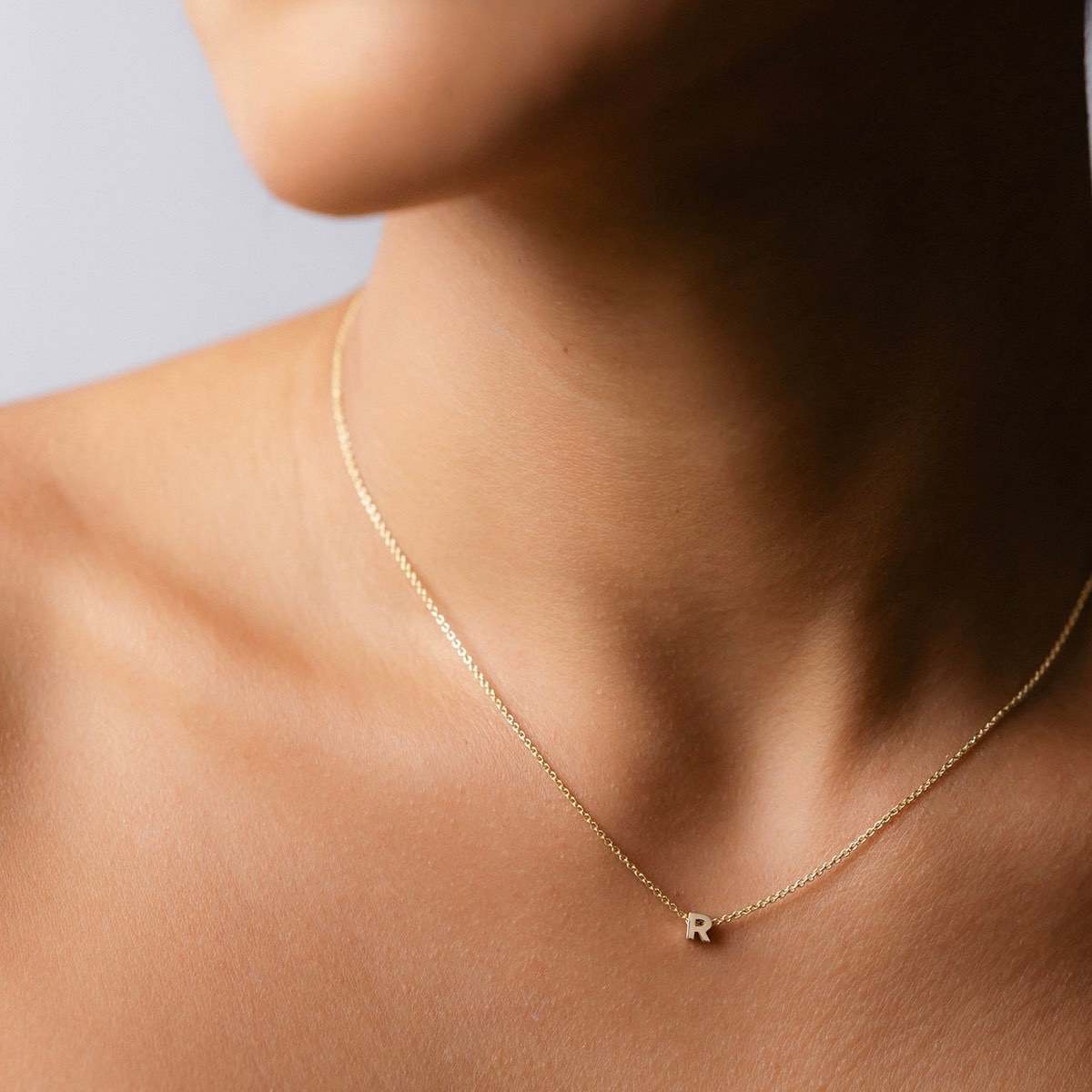 Hand finished solid gold letter necklace: Close up of a model wearing our beautiful 9ct yellow gold Tiny Letter R Charm Necklace with a 40cm cable chain