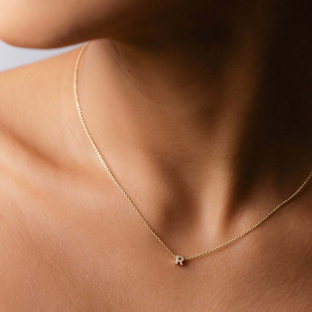 Hand finished solid gold letter necklace: Close up of a model wearing our beautiful 9ct yellow gold Tiny Letter R Charm Necklace with a 40cm cable chain