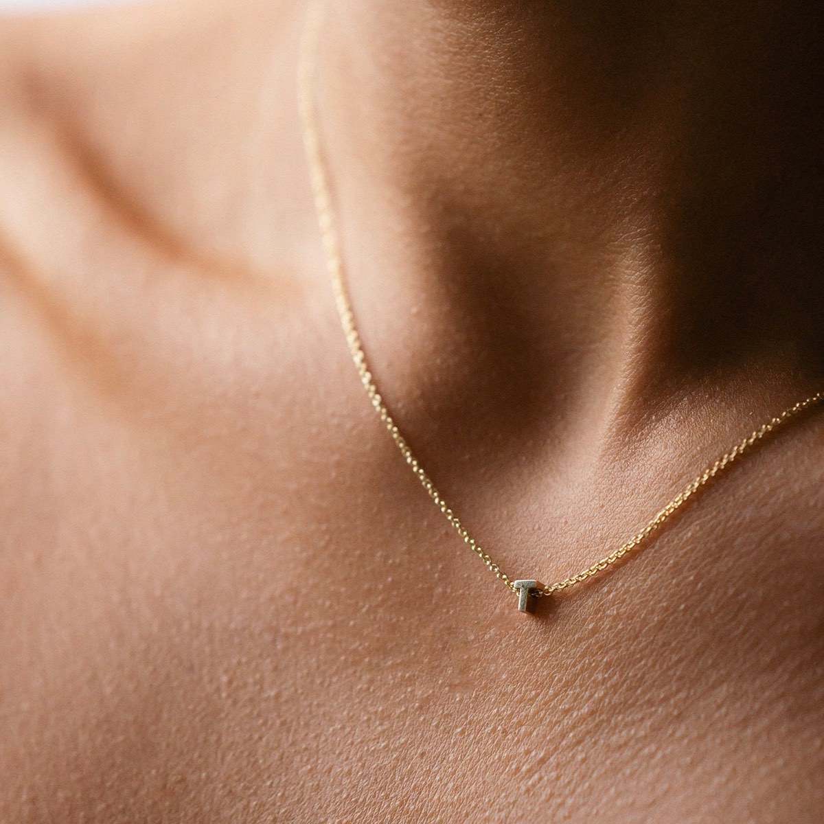 Hand finished solid gold letter necklace: Close up of a model wearing our beautiful 9ct yellow gold Tiny Letter T Charm Necklace with a 40cm cable chain