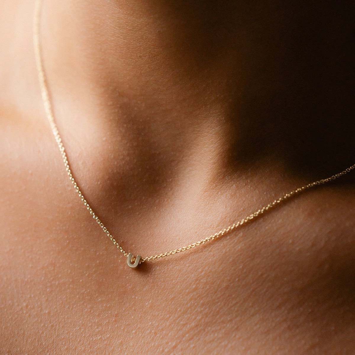 Hand finished solid gold letter necklace: Close up of a model wearing our beautiful 9ct yellow gold Tiny Letter U Charm Necklace with a 40cm cable chain