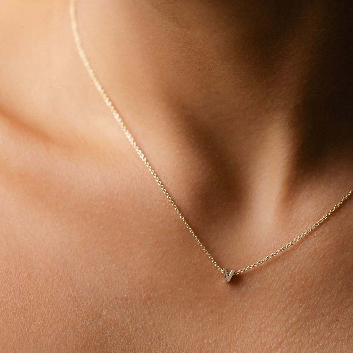 Hand finished solid gold letter necklace: Close up of a model wearing our beautiful 9ct yellow gold Tiny Letter V Charm Necklace with a 40cm cable chain