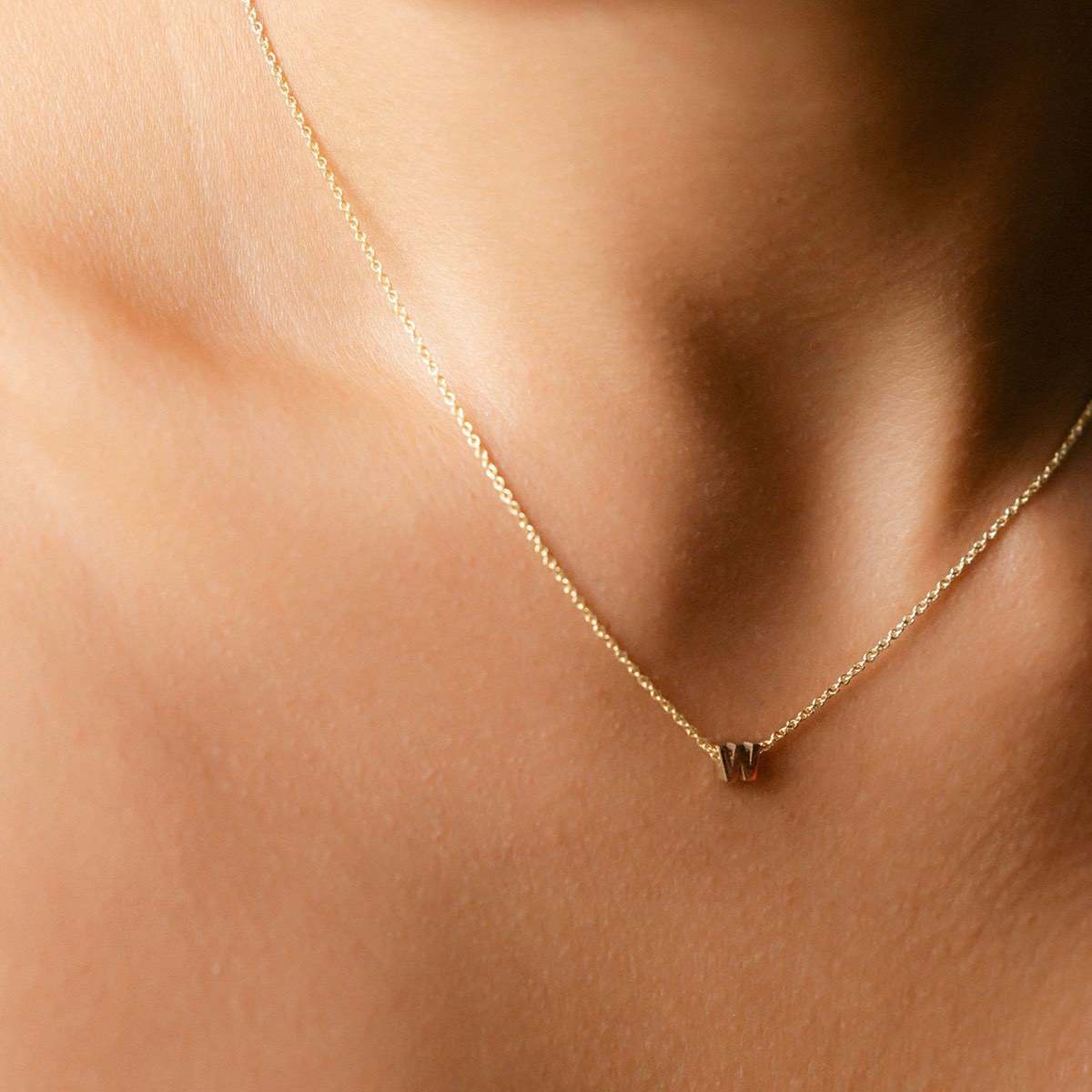 Hand finished solid gold letter necklace: Close up of a model wearing our beautiful 9ct yellow gold Tiny Letter W Charm Necklace with a 40cm cable chain