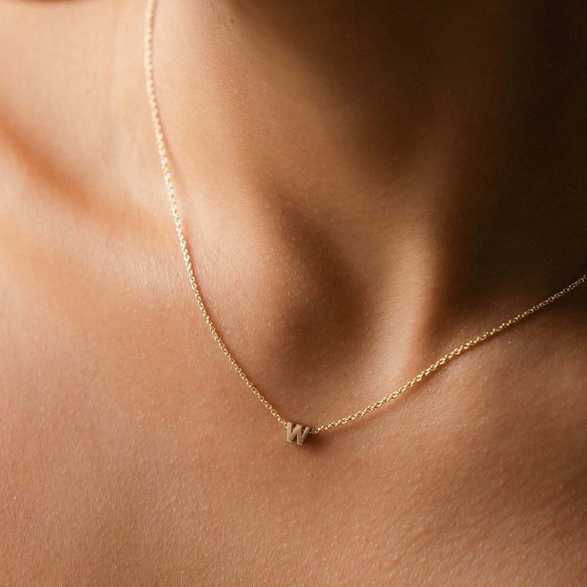 Hand finished solid gold letter necklace: Close up of a model wearing our beautiful 9ct yellow gold Tiny Letter W Charm Necklace with a 40cm cable chain