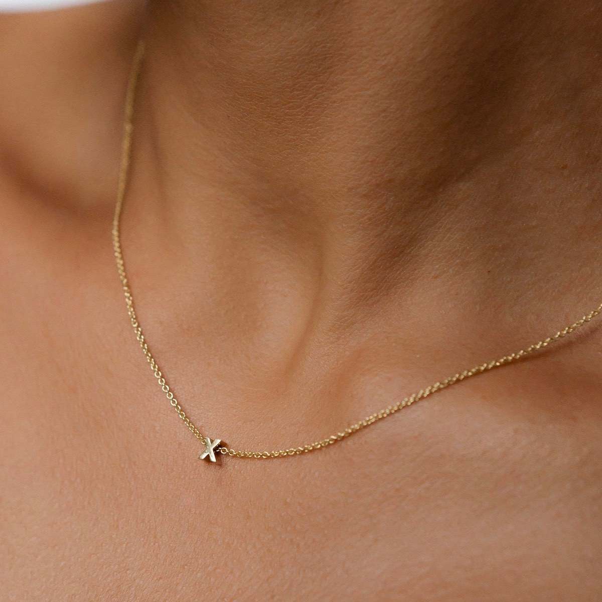 Hand finished solid gold letter necklace: Close up of a model wearing our beautiful 9ct yellow gold Tiny Letter X Charm Necklace with a 40cm cable chain