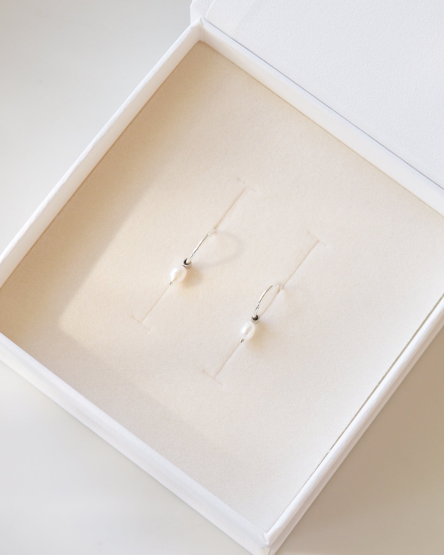 Pearl earrings in a white jewelry box on a white background