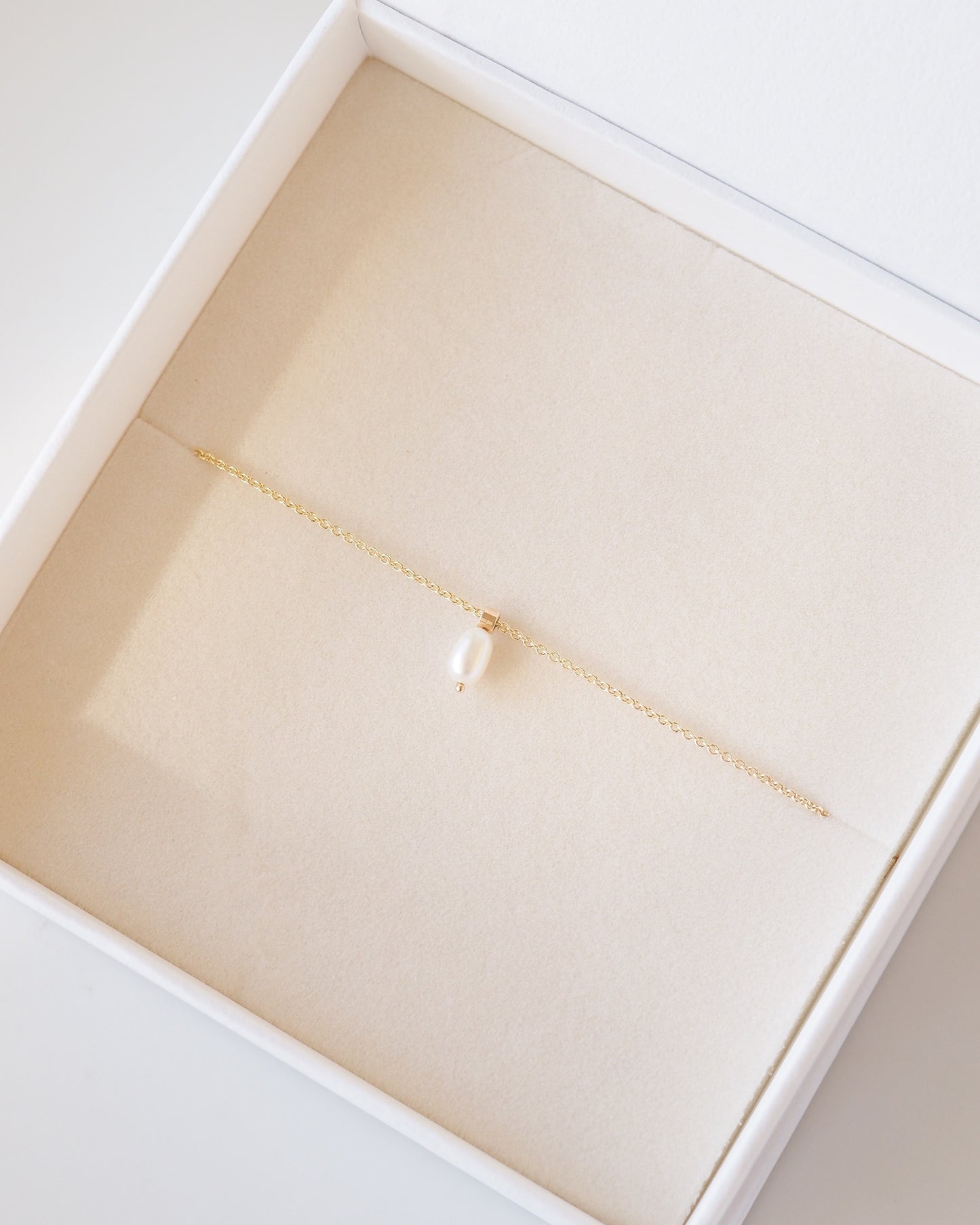 Gold necklace with a pearl pendant in an open jewelry box on a light background