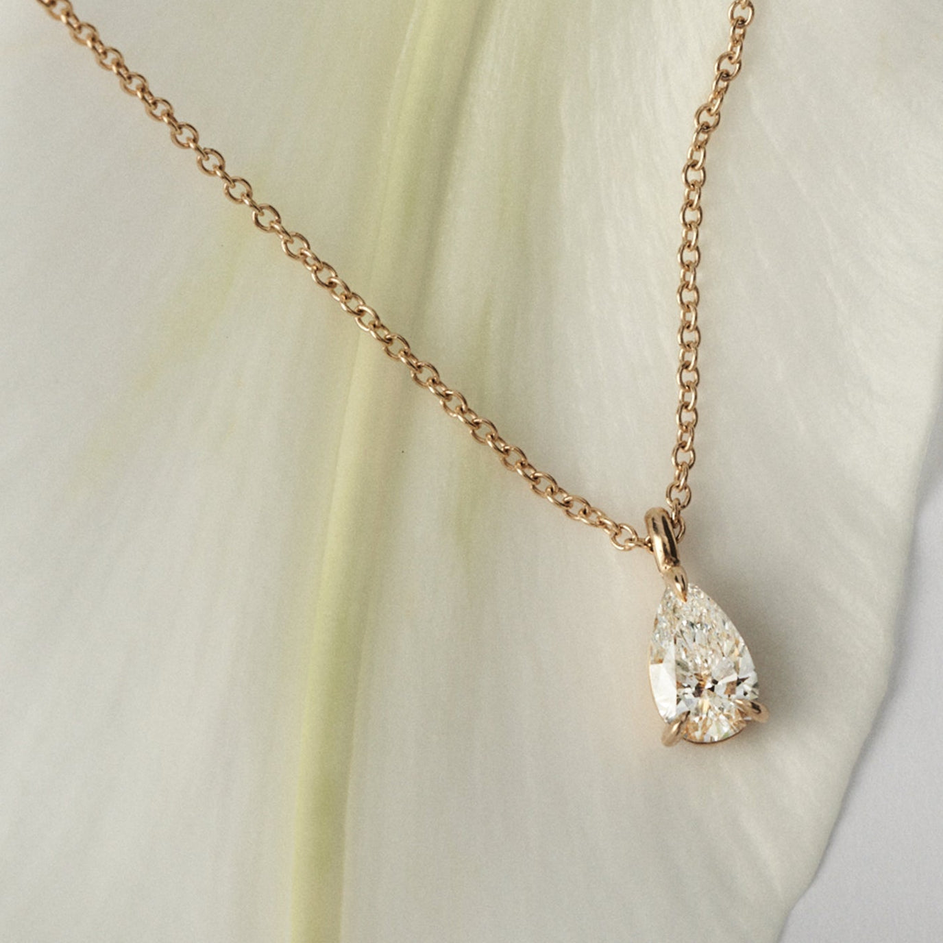 Gold necklace with a pear shaped diamond pendant on a light fabric background