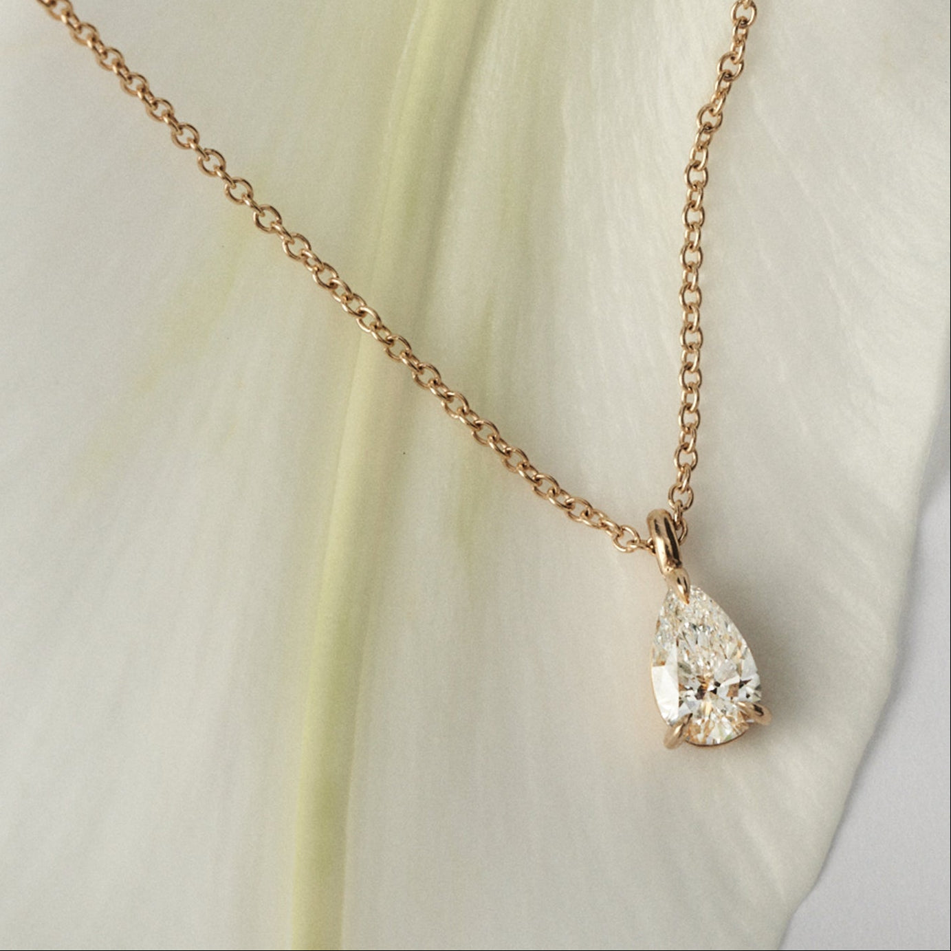Gold necklace with a pear shaped diamond pendant on a light fabric background