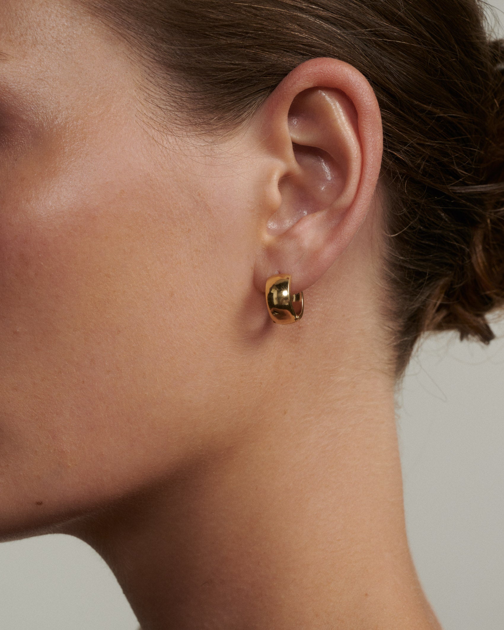 Gold hoop earring worn by a person with a neutral background