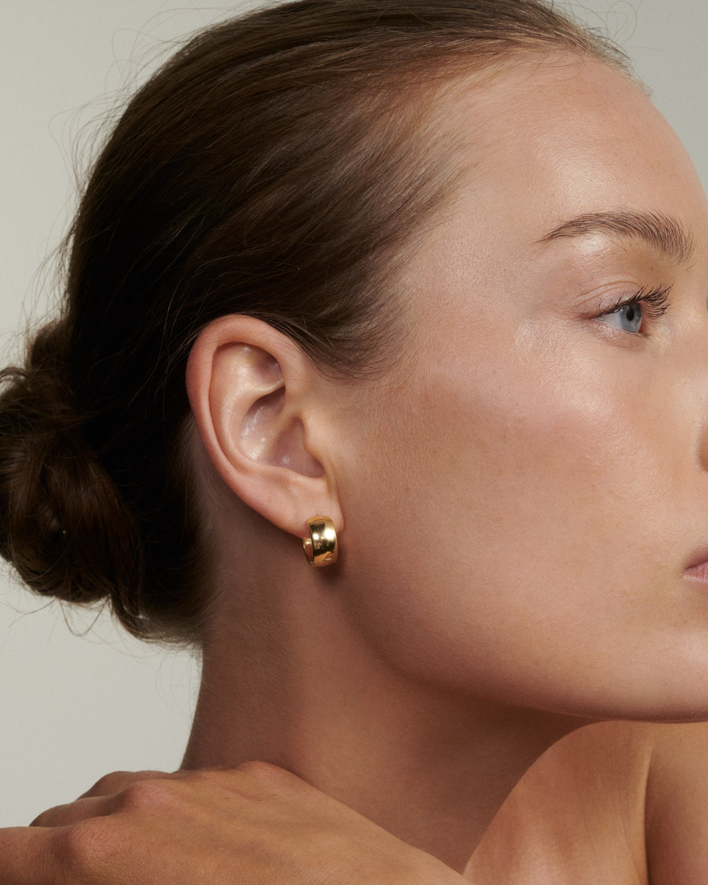 Close-up of a person wearing a gold earring with a neutral background