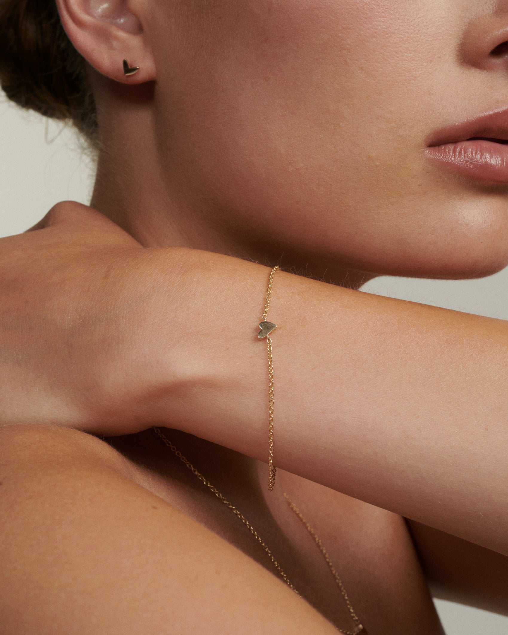 Close-up of a person wearing a delicate gold bracelet on a neutral background