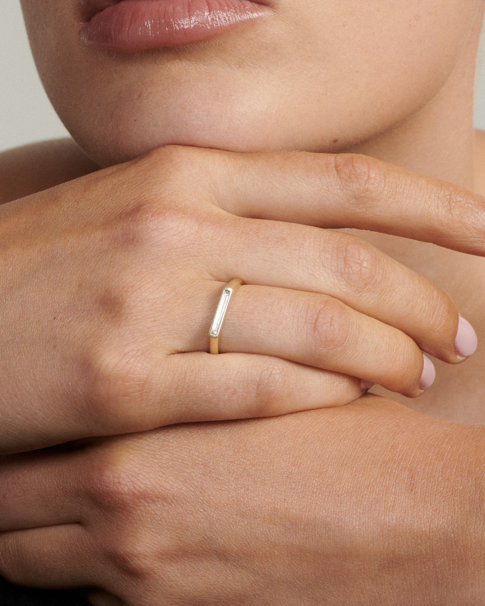 Close-up of a hand wearing a gold ring with a white stone.