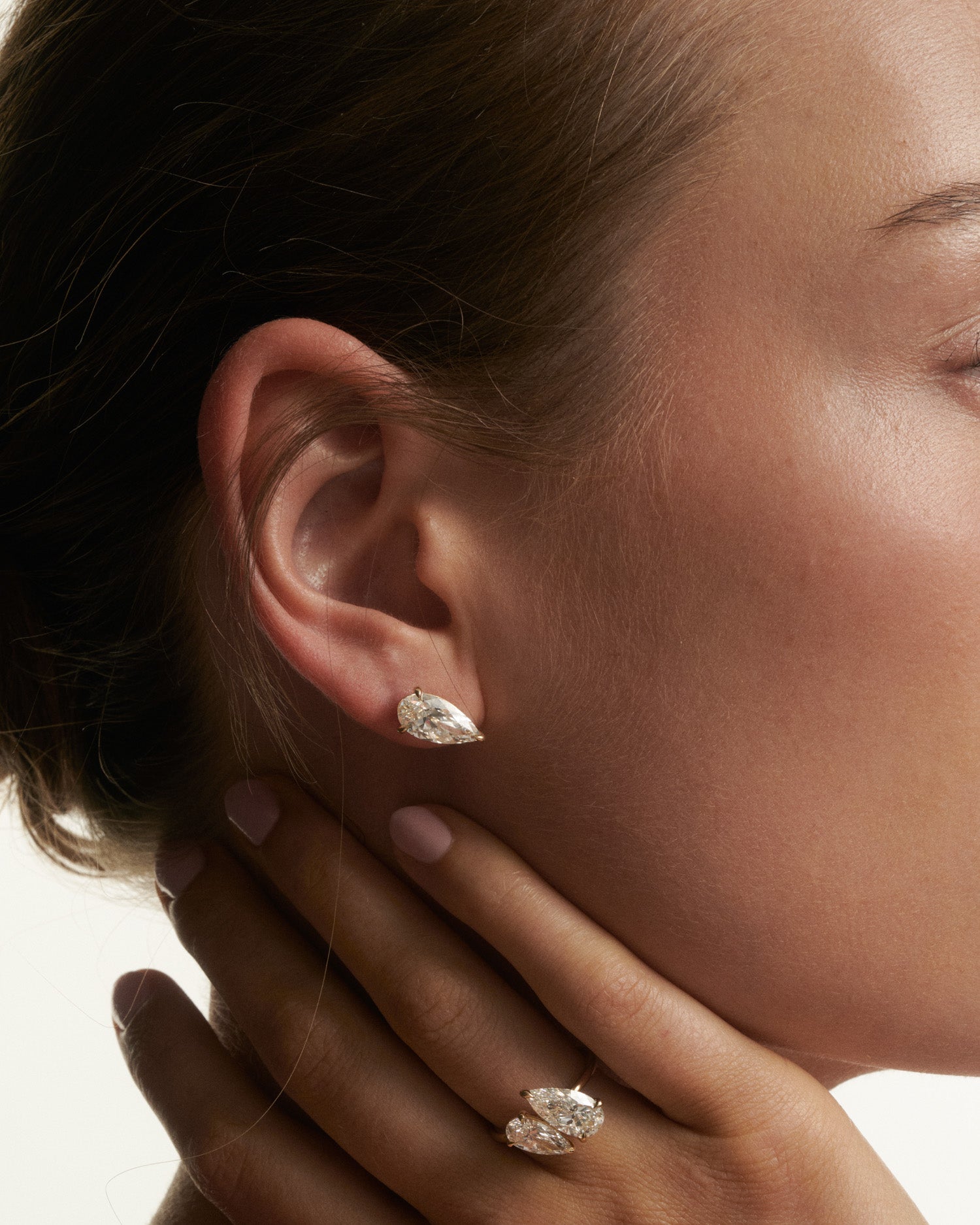 Close-up of a woman wearing diamond earrings with a hand touching her face.
