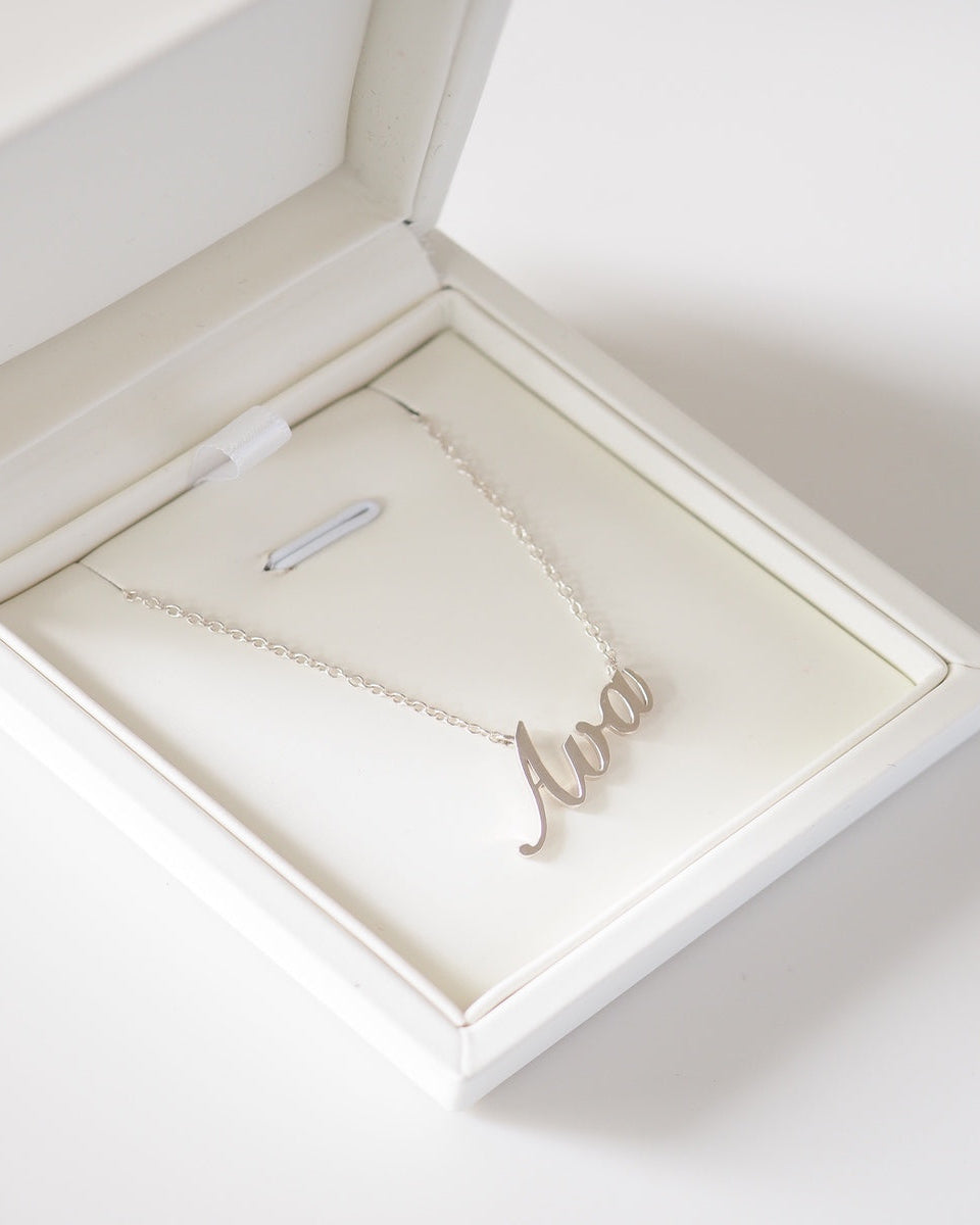 Silver necklace with 'Ava' pendant in an open jewelry box on a light background