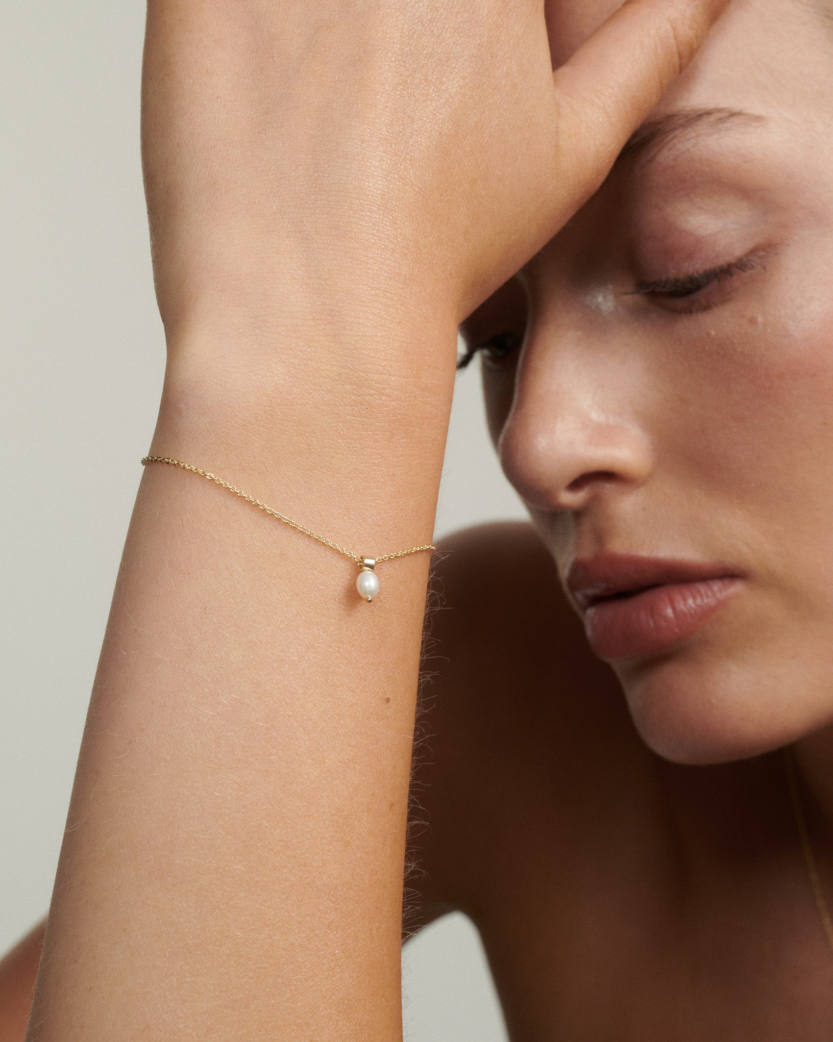 Woman wearing a delicate gold bracelet with a pearl on a neutral background