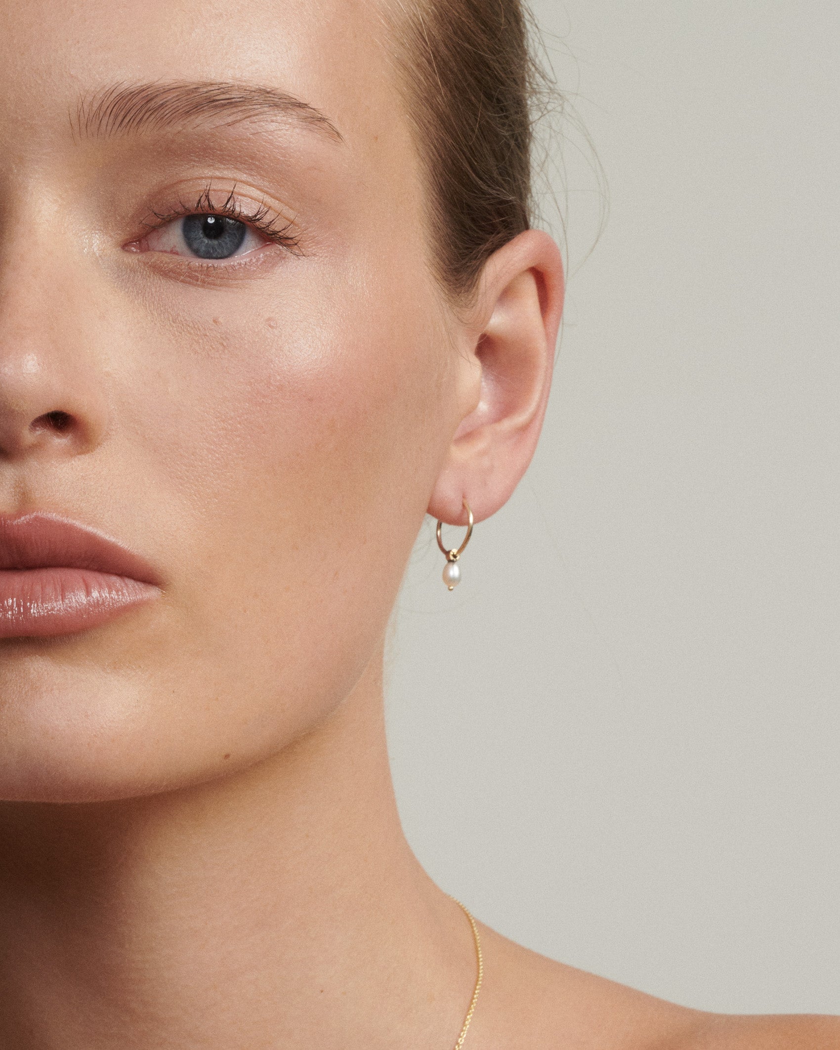 Close-up of a person wearing a gold hoop earring against a neutral background