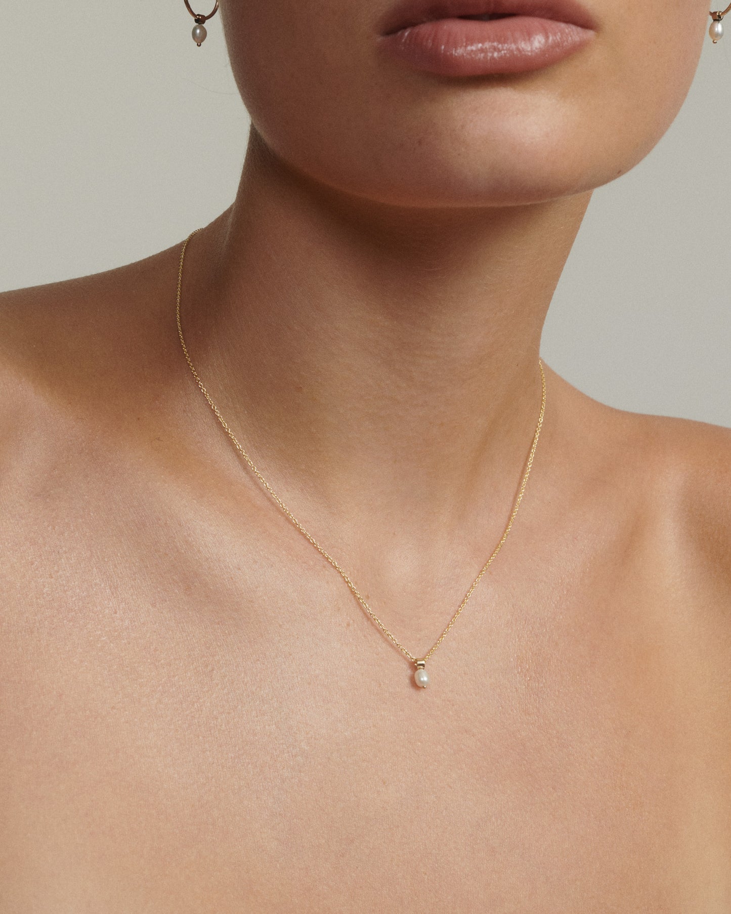 Gold necklace with a pearl pendant on a neutral background