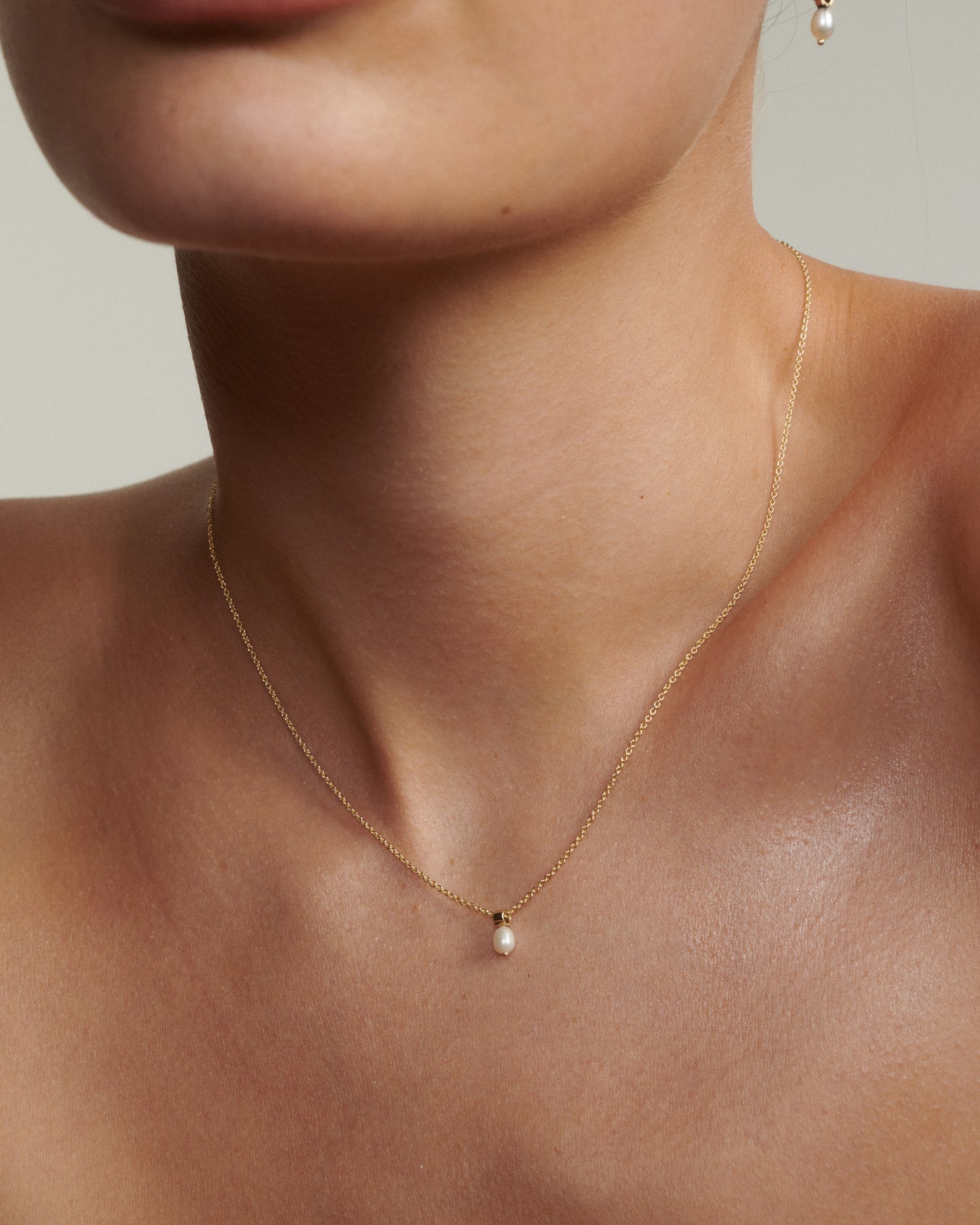 Close-up of a person wearing a delicate gold necklace with a pearl pendant.