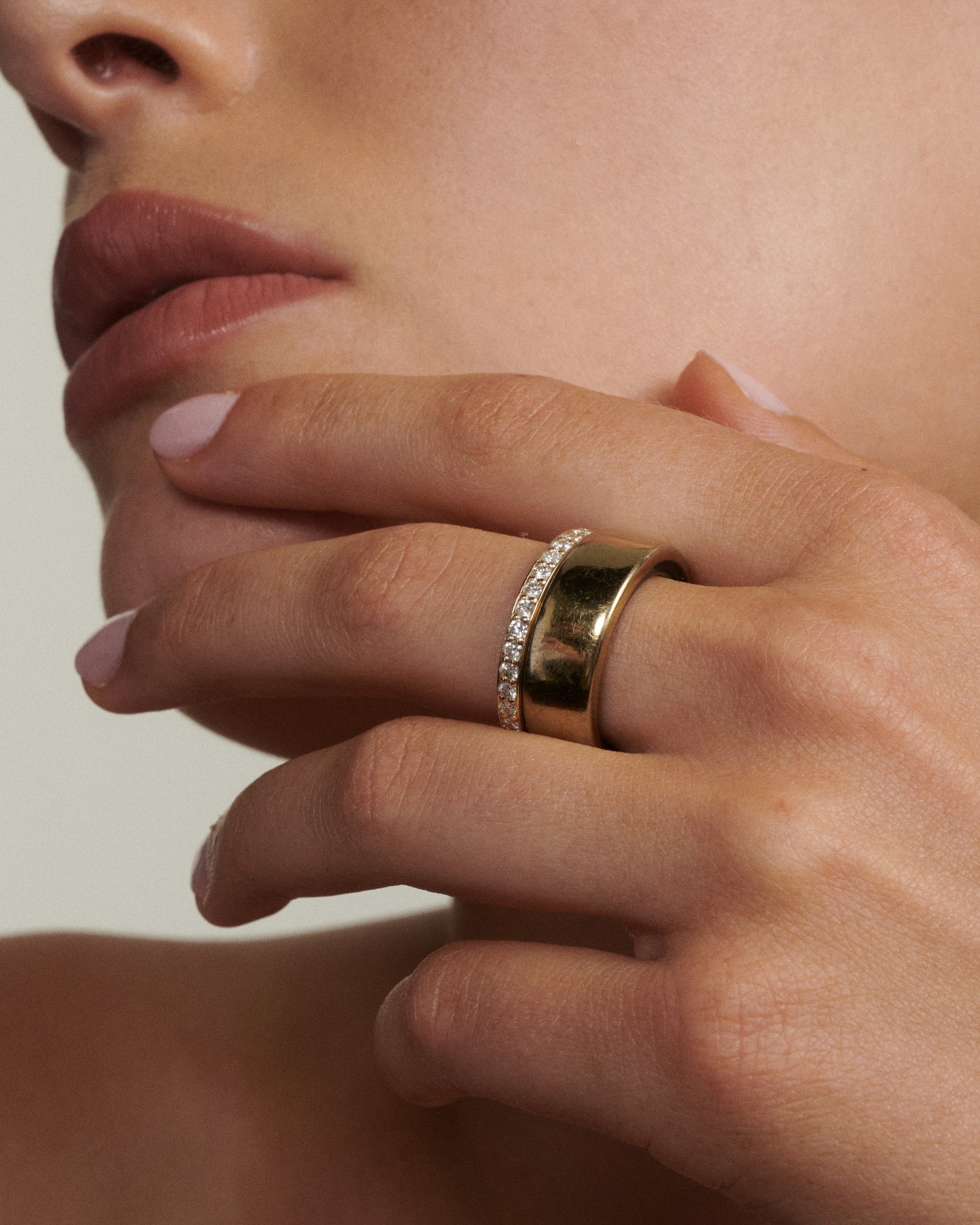 Close-up of a hand wearing two gold rings with a neutral background