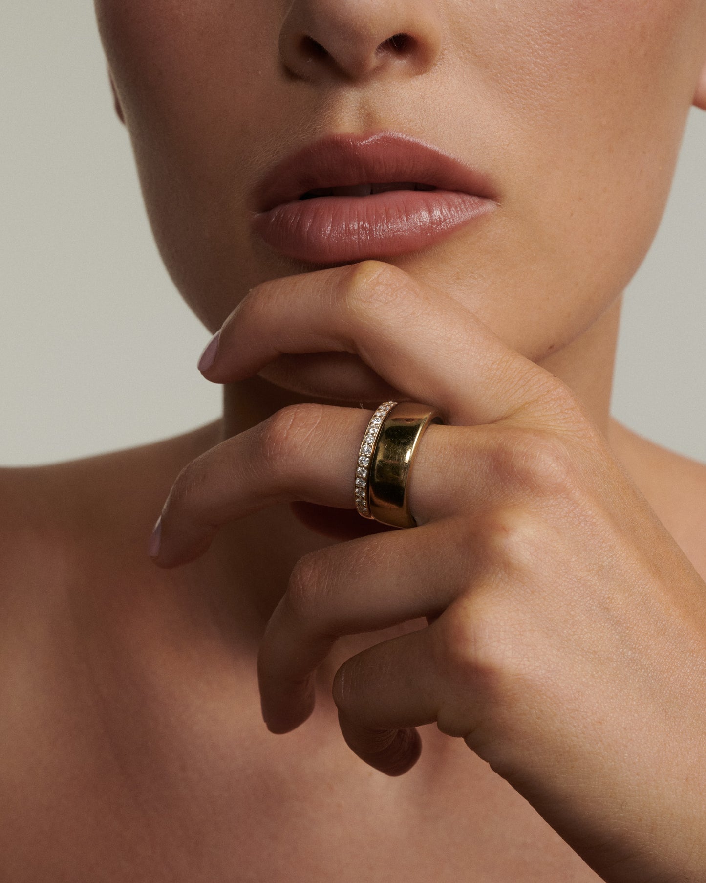 Close-up of a person wearing a gold ring on their finger with a neutral background