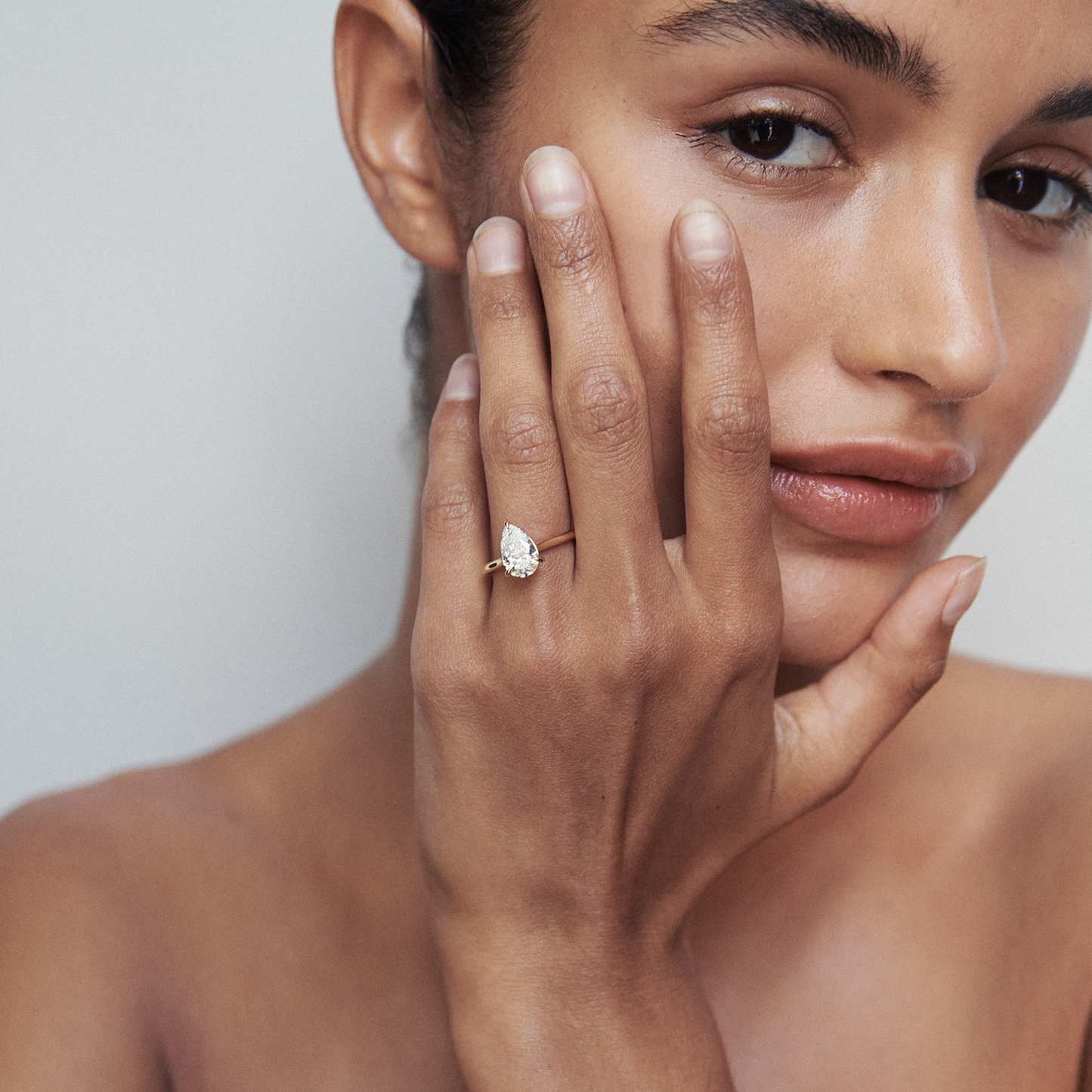 Close-up of a woman showcasing a luxurious pear-shaped diamond ring on her finger, with minimalistic elegance and soft lighting.