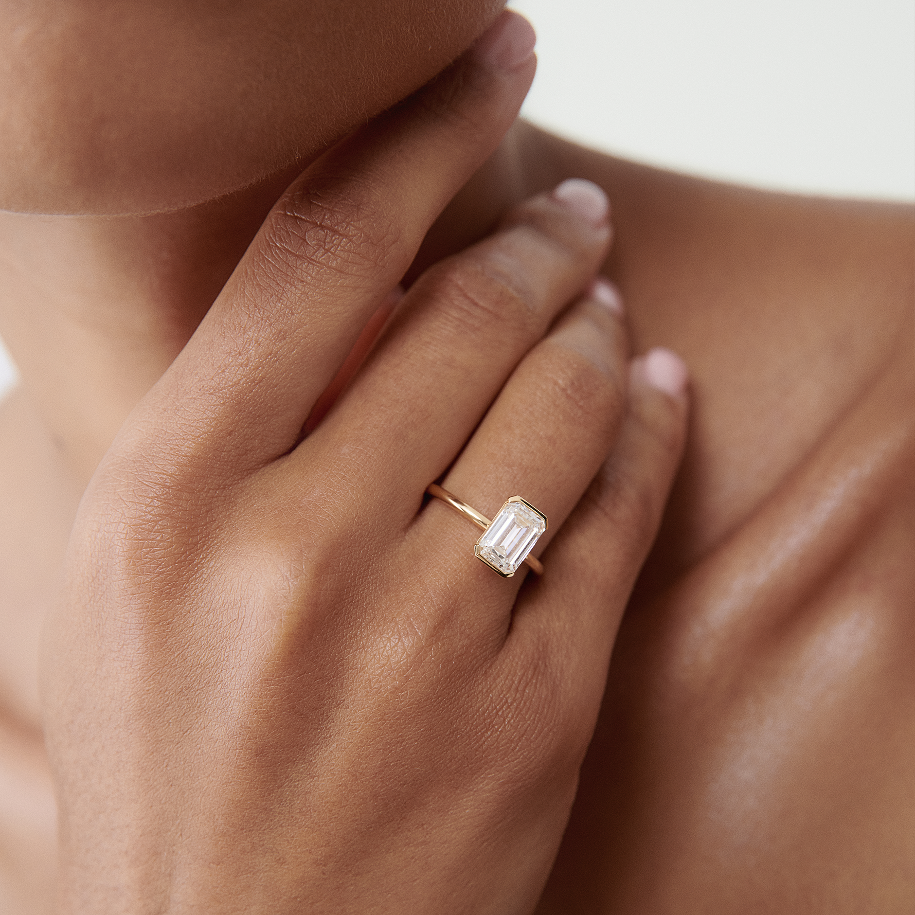 Elegant hand wearing a luxurious emerald-cut diamond ring on a slender gold band, highlighting high-end jewellery style.