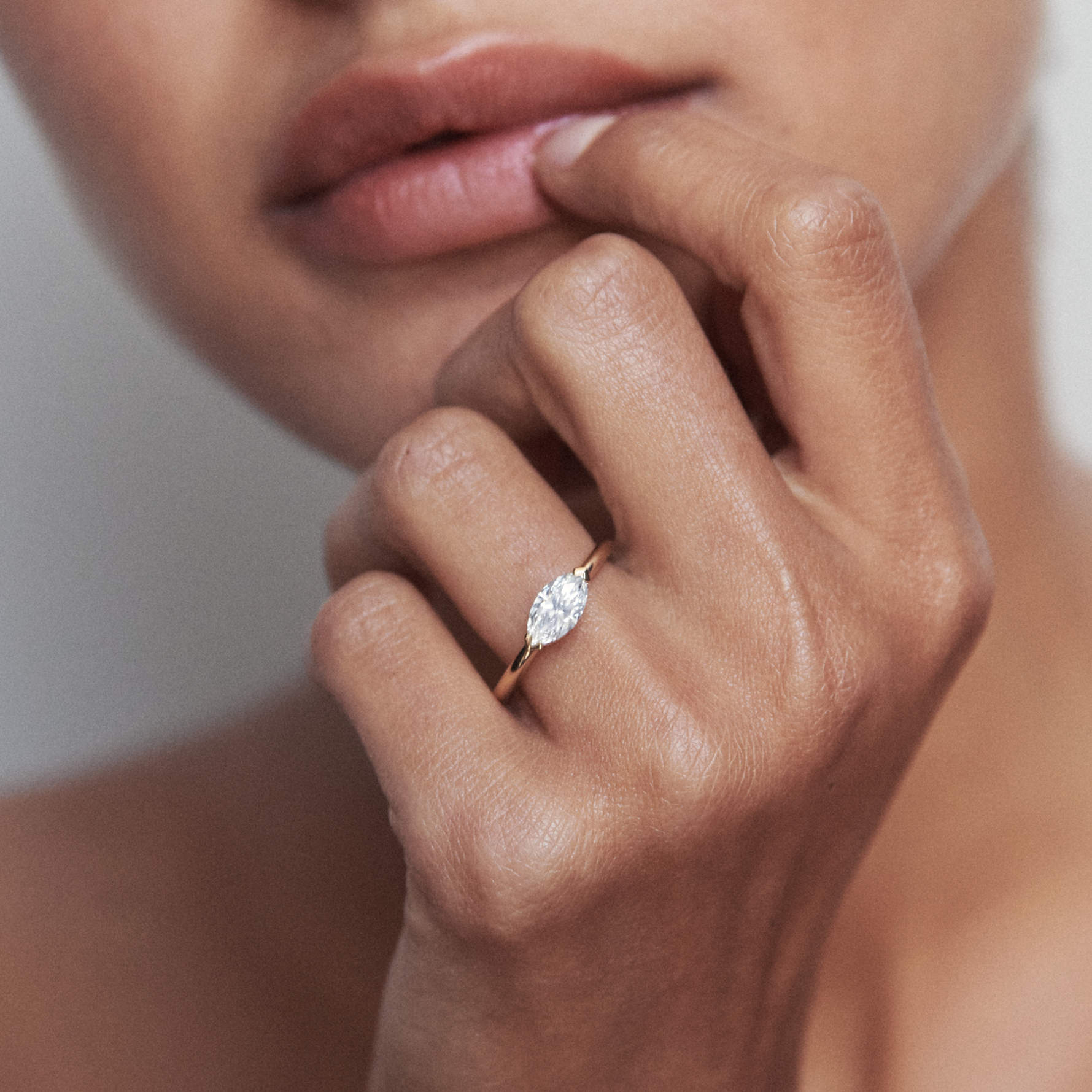 Close-up of a woman's hand wearing an elegant gold ring with a marquise-cut diamond, held near her lips. Luxury jewellery style.