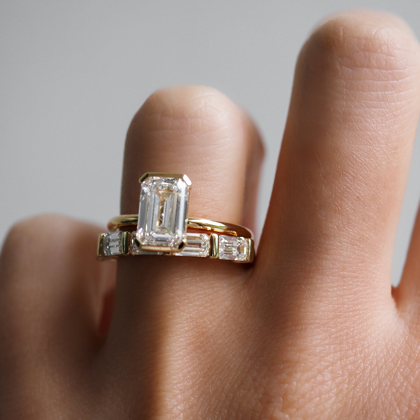 Close-up of a hand wearing two rings; one with a large emerald-cut diamond and another with rectangular diamonds in a gold setting.
