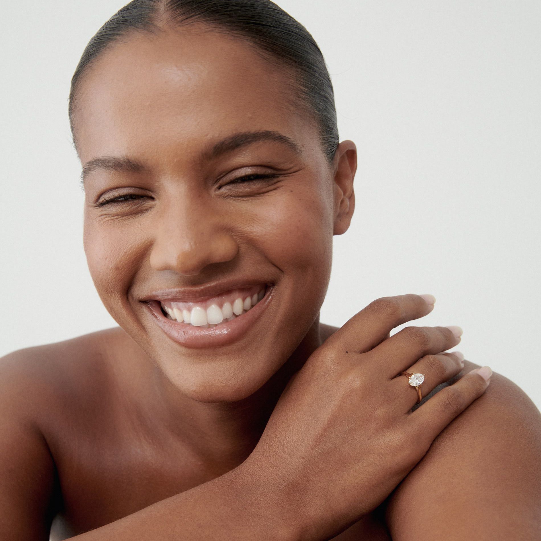 Smiling woman wearing a solitaire diamond ring. Hair tied back, showing confidence and elegance. Perfect for luxury jewellery marketing.