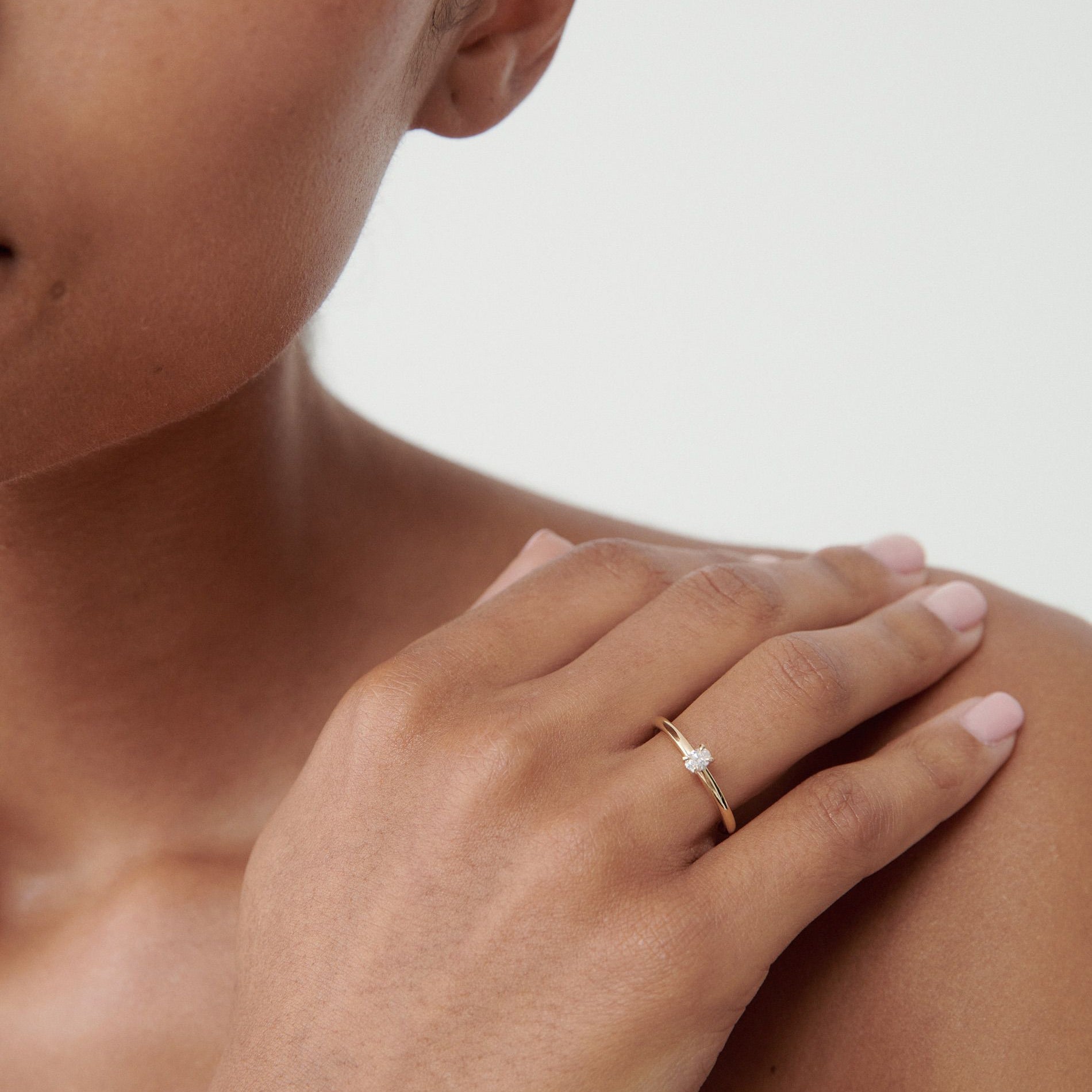 A close-up of a woman's hand wearing a delicate gold ring with a small diamond, set against a soft, neutral background.